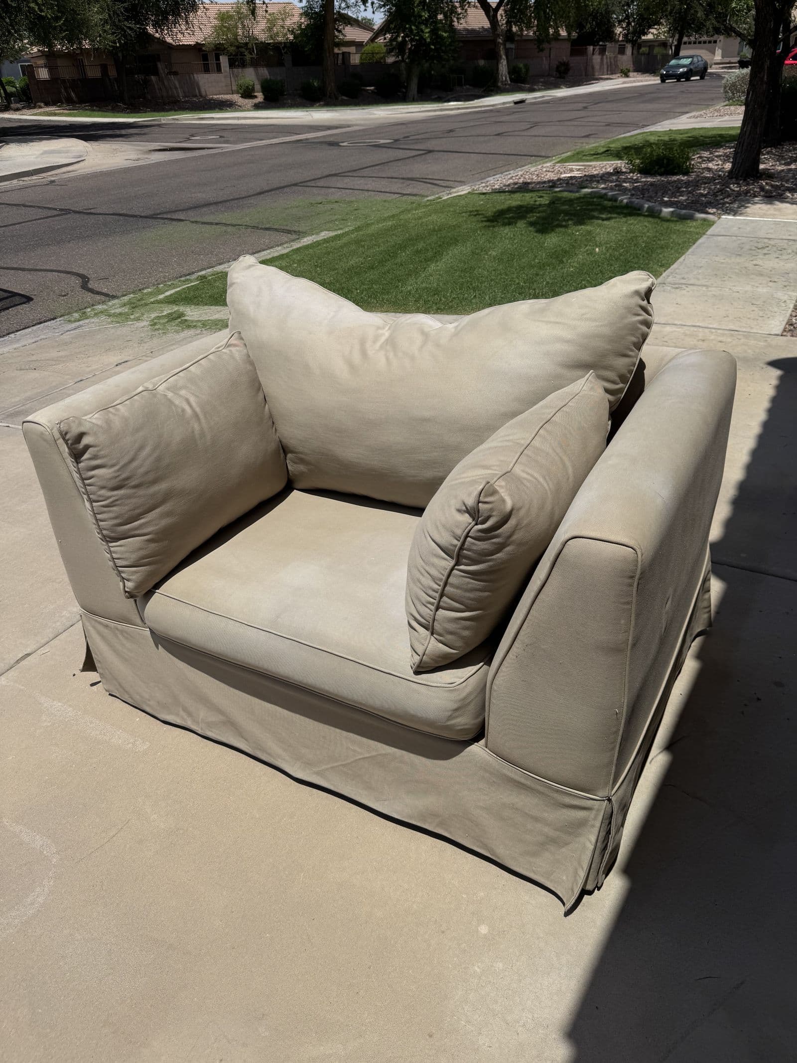 Oversized beige armchair on a driveway ready for junk removal pickup