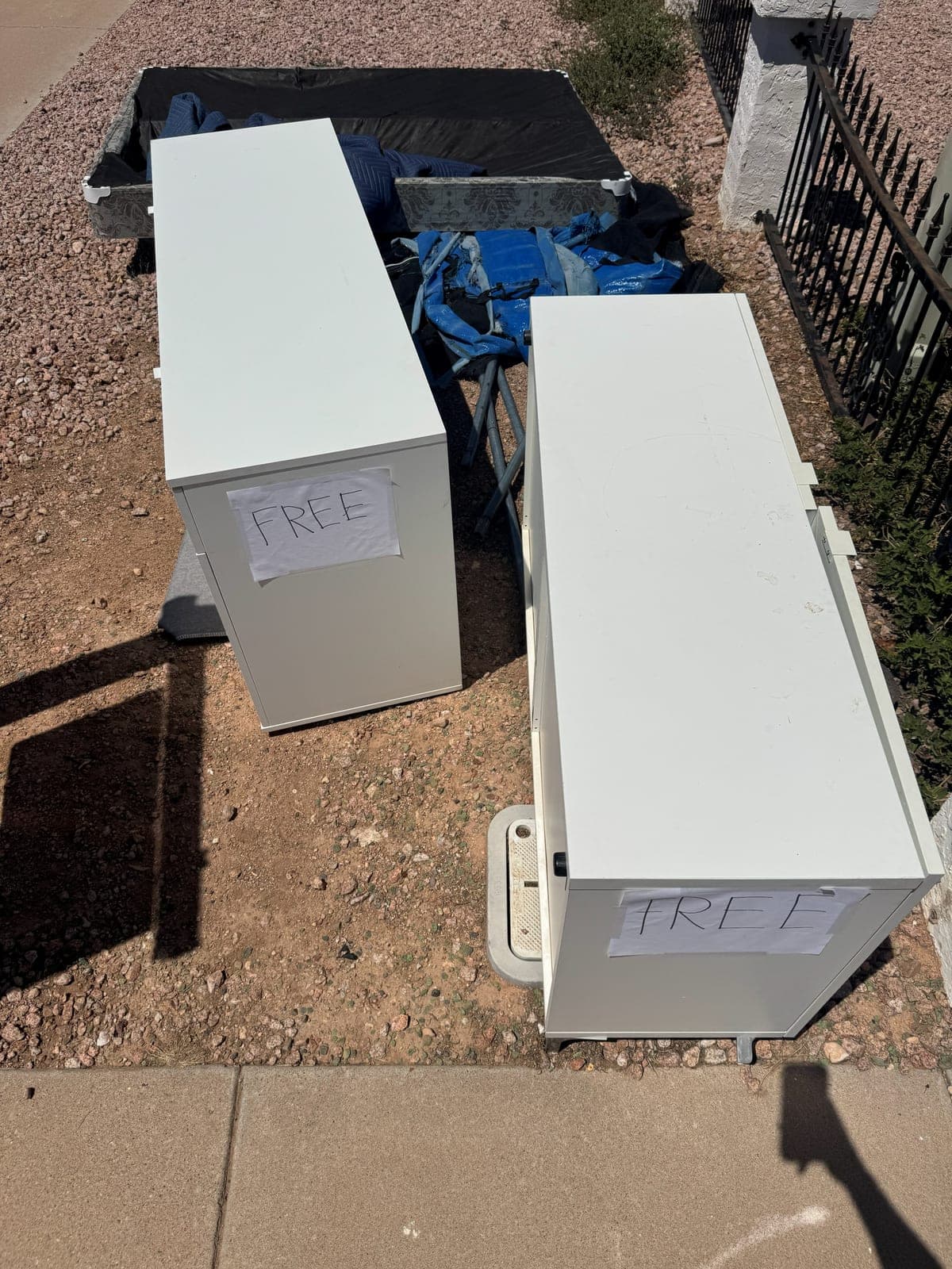 Two white storage cabinets taped with free signs sitting at the curb before a junk removal pickup